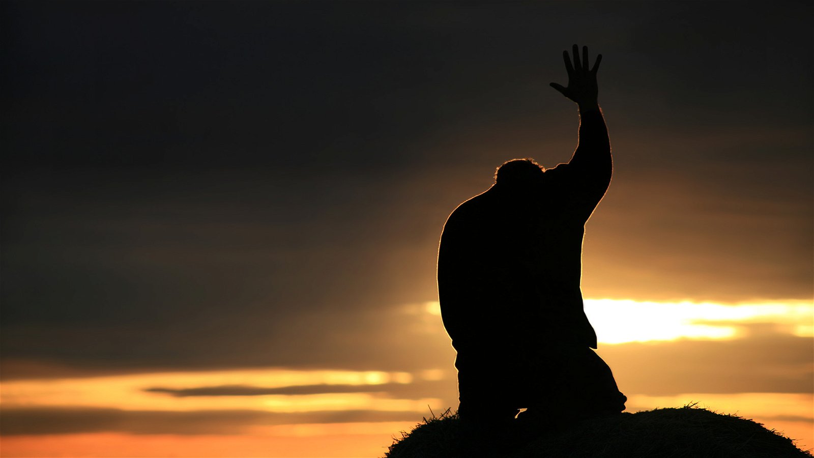Man kneeling with hand raised at sunset